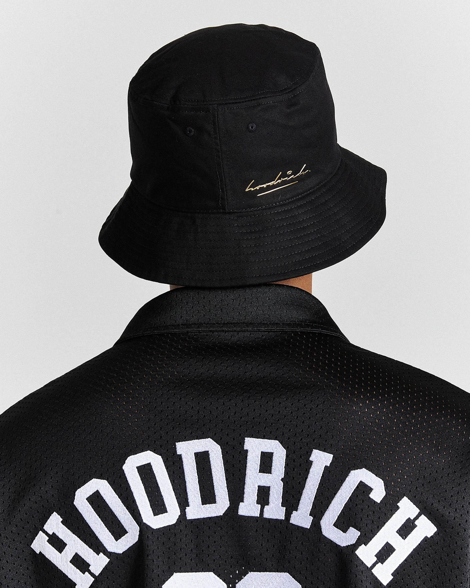 Person wearing a black bucket hat with a brand logo and a black jacket with 'HOODRICH' text.