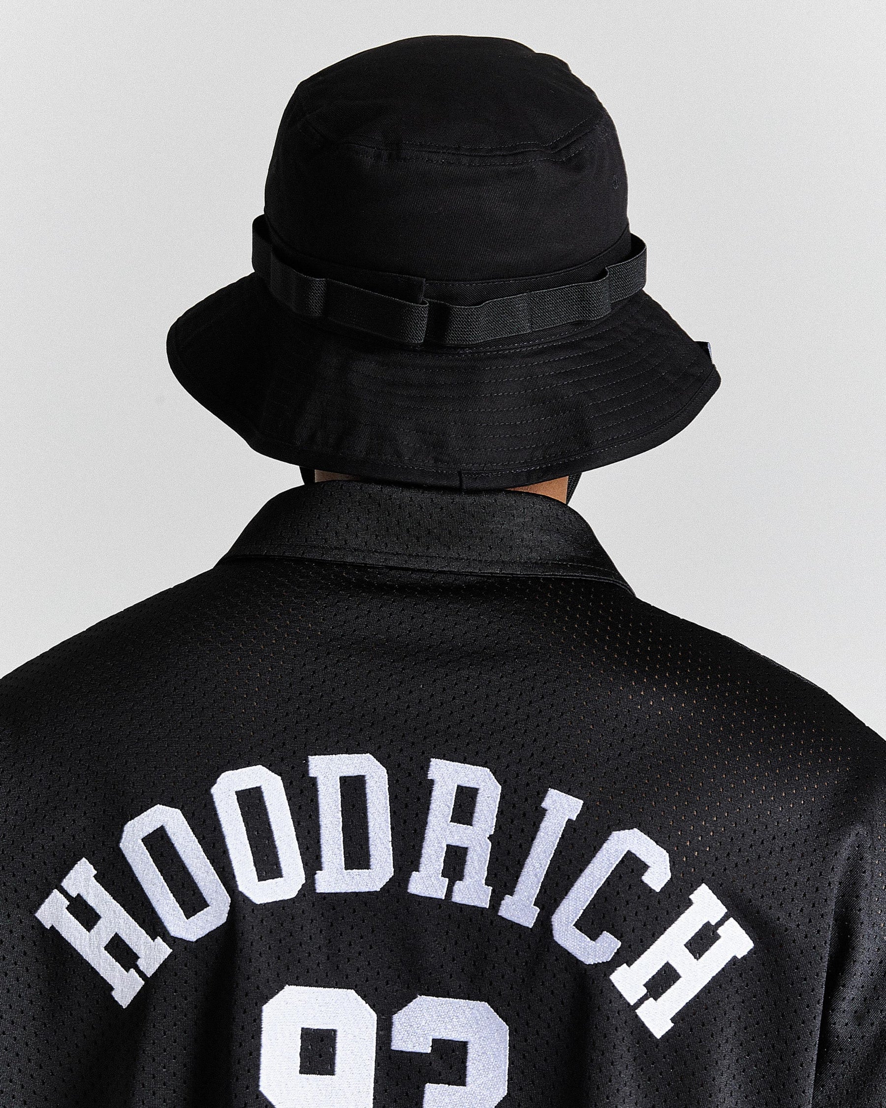 Person wearing a black bucket hat and black jacket with 'Hoodrich' text on a light gray background
