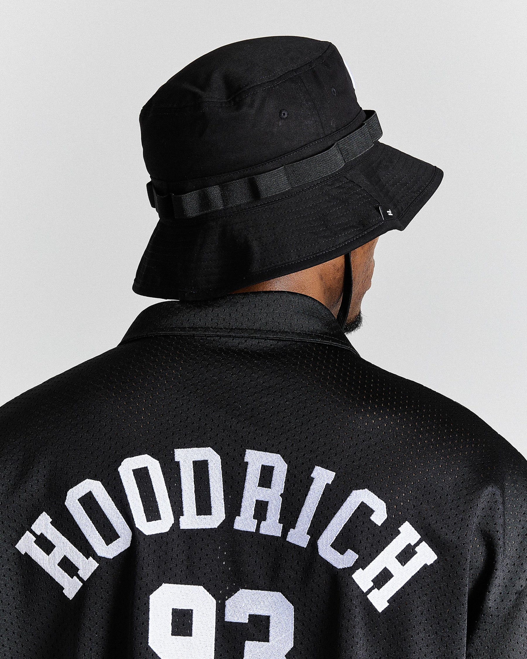 Person wearing a black bucket hat and black jacket with 'Hoodrich' text on a light gray background