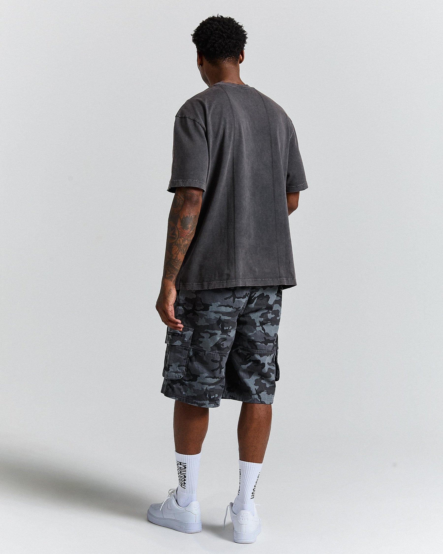 Person wearing a grey t-shirt and camouflage shorts on a white background