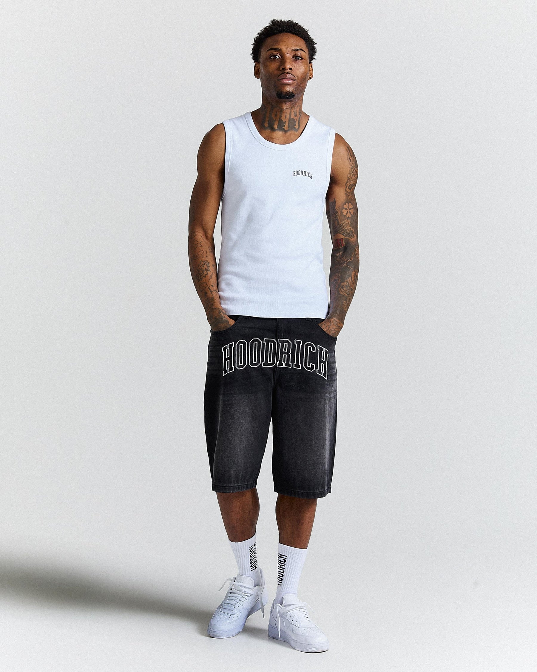 Man wearing a white tank top and black shorts with 'Hoodrich' branding on a light gray background