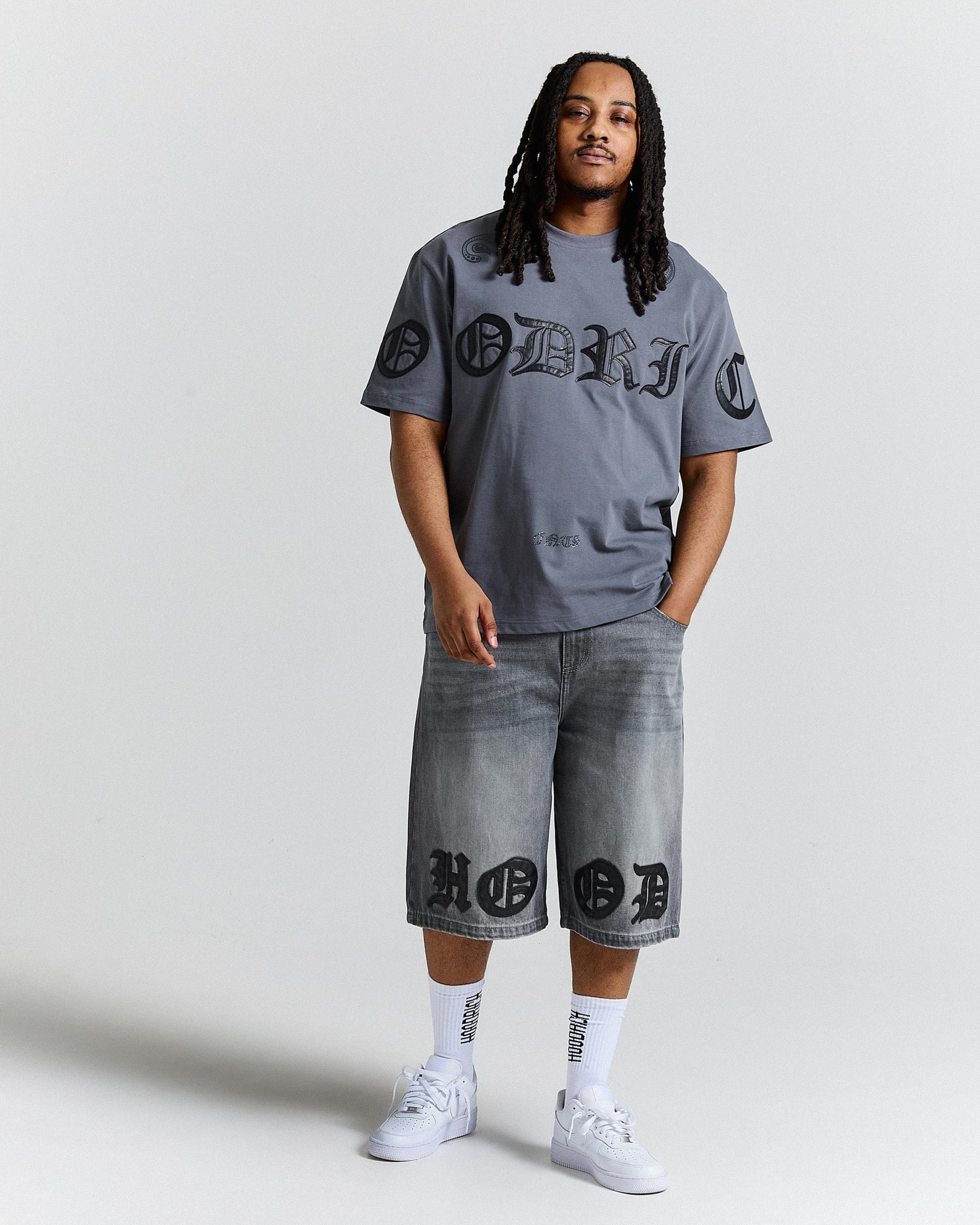 Person wearing a gray t-shirt and shorts with branding, standing against a plain background