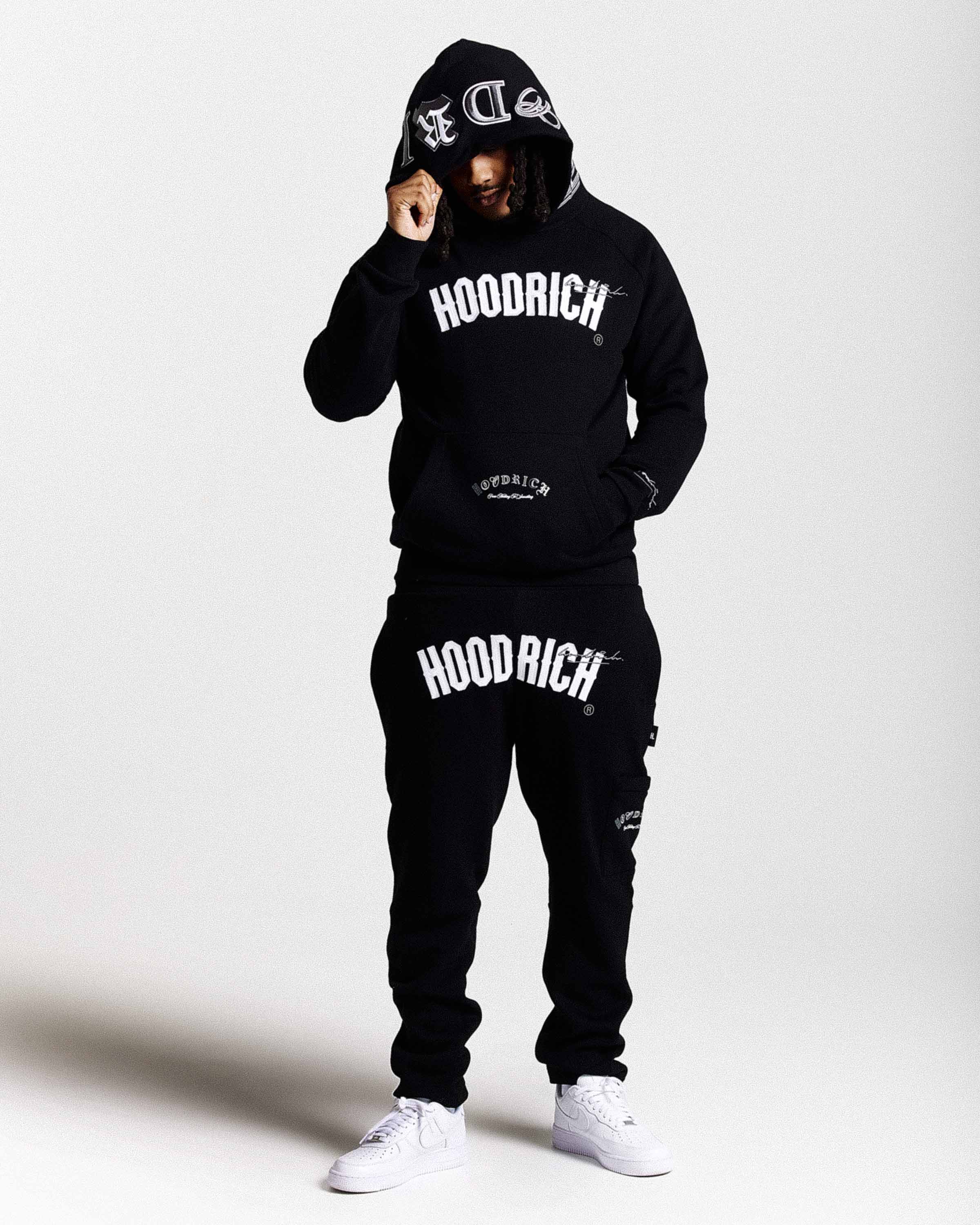 Person wearing a black 'Hoodrich' hoodie and pants on a white background