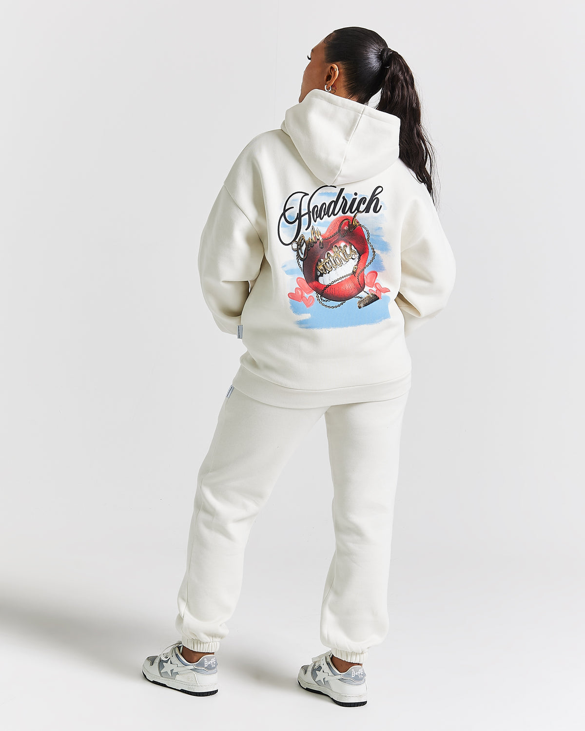 Displays a model wearing the White 'Hoodrich' branded women's Grillz Full Tracksuit 